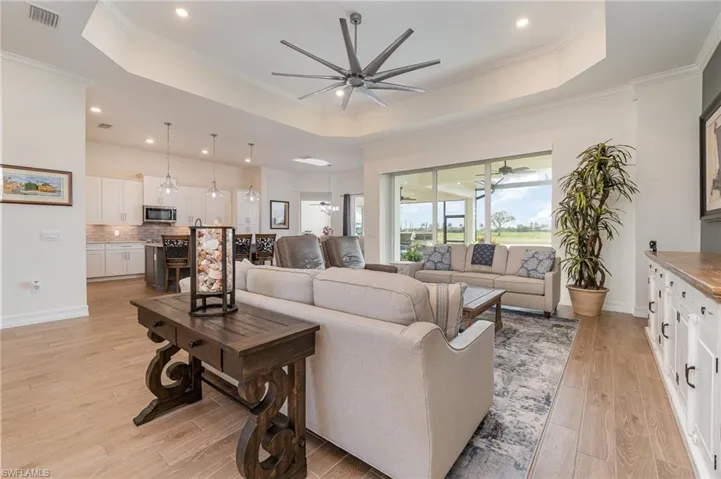 Living room featuring a tray ceiling, crown molding, tiled flooring, and ceiling fan
