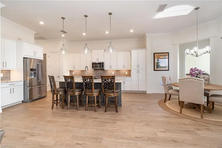 Kitchen with stainless steel appliances, a kitchen island with sink, decorative fixtures, white cabinets, and light tiled floors