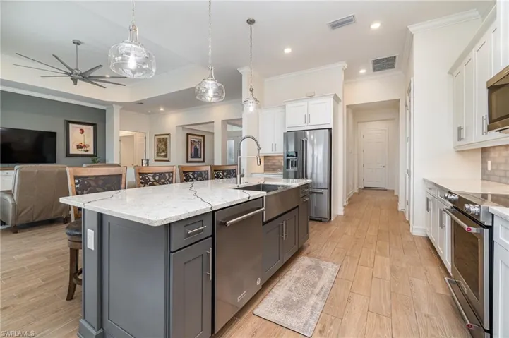 Kitchen featuring decorative backsplash, white cabinetry, stainless steel appliances, and a kitchen island with sink
