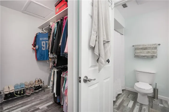 Full bathroom with curtained shower, dark wood-style floors, and a spacious closet