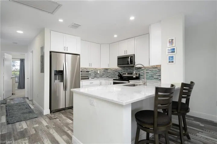 Kitchen with appliances with stainless steel finishes, white cabinets, light stone countertops, backsplash, and recessed lighting