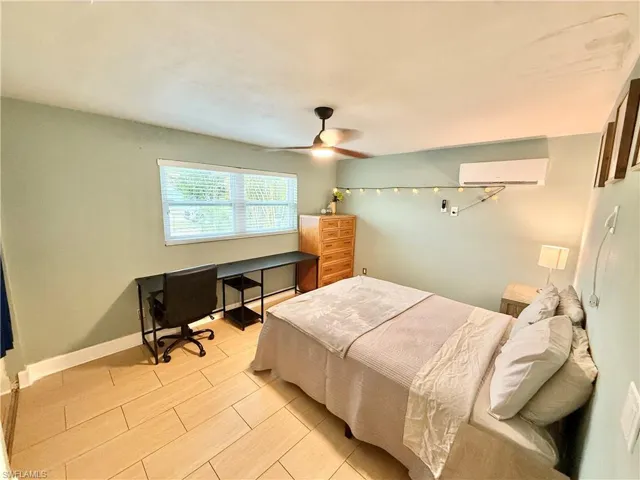 Bedroom featuring a wall mounted air conditioner, an office area, a ceiling fan, baseboards, and wood tiled floors