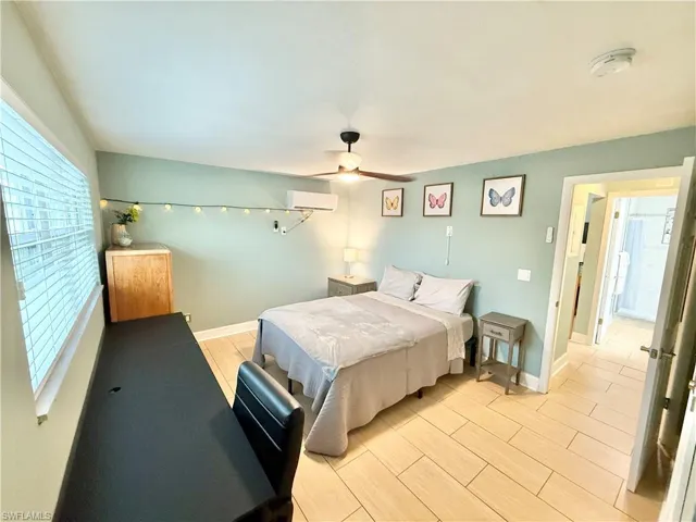 Bedroom featuring multiple windows, an AC wall unit, baseboards, and a ceiling fan