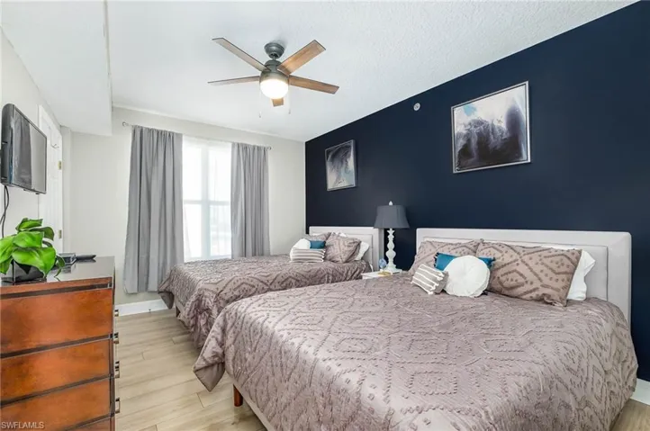Bedroom featuring light wood-style floors, a ceiling fan, an accent wall, and a textured ceiling