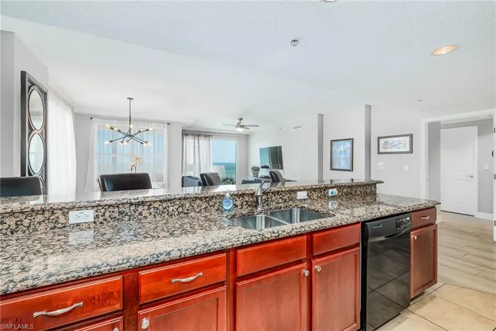 Kitchen with light stone counters, dishwasher, a chandelier, dark brown cabinets, and ceiling fan