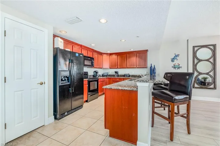 Kitchen with black appliances, a kitchen bar, a peninsula, light stone countertops, and a textured ceiling