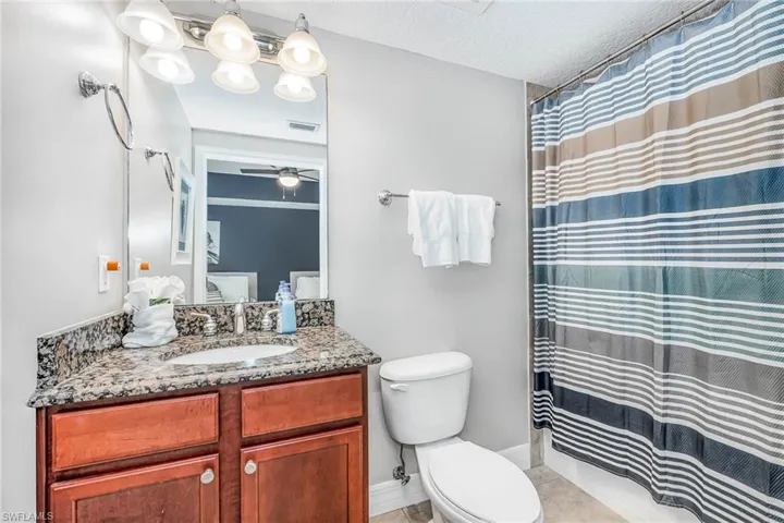 Full bath featuring curtained shower, vanity, a textured ceiling, light tile patterned flooring, and a ceiling fan