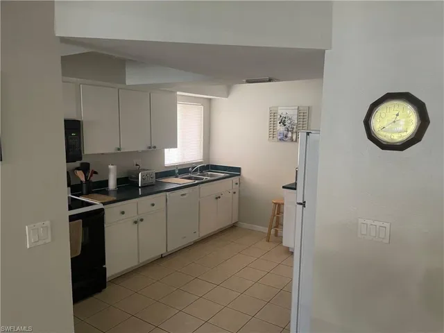 Kitchen featuring dark countertops, white cabinets, black appliances, and light tile patterned floors