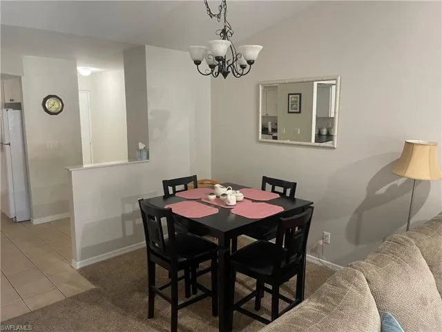 Dining room featuring vaulted ceiling, light colored carpet, light tile patterned floors, and suspended lighting