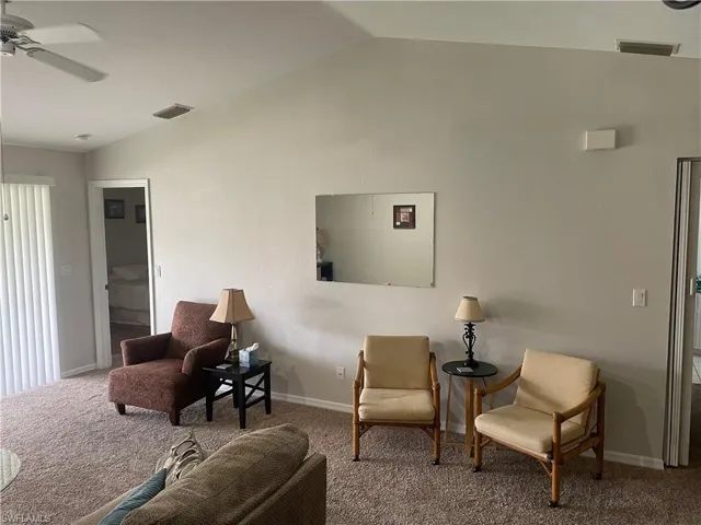 Living area featuring vaulted ceiling, ceiling fan, and carpet flooring