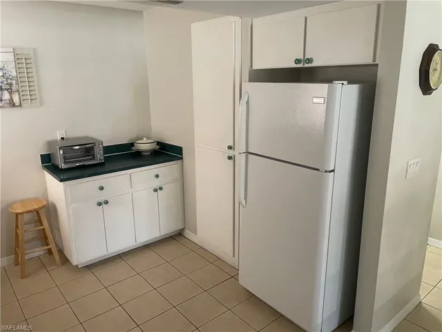 Kitchen featuring freestanding refrigerator, dark countertops, white cabinets, and light tile patterned floors