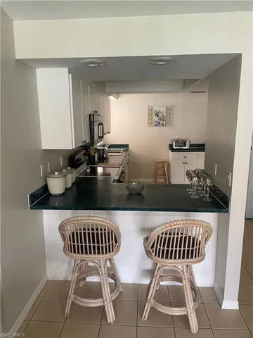 Kitchen with white cabinets, dark countertops, a breakfast bar area, and range with electric stovetop