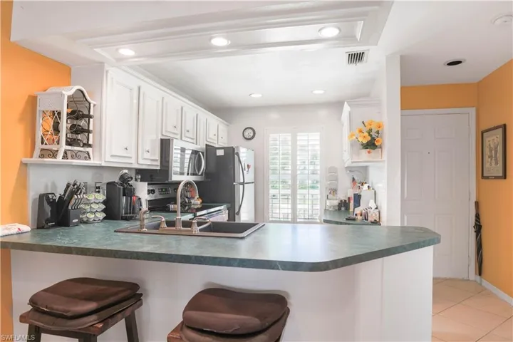 Kitchen featuring stainless steel appliances, kitchen peninsula, a kitchen breakfast bar, and white cabinetry