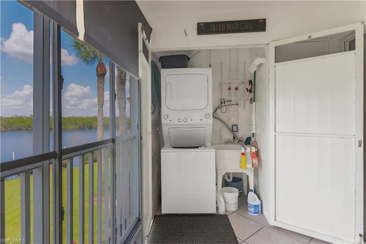 Clothes washing area with a water view, stacked washer and dryer, and light tile patterned floors