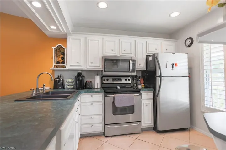 Kitchen with light tile patterned flooring, stainless steel appliances, sink, and white cabinetry