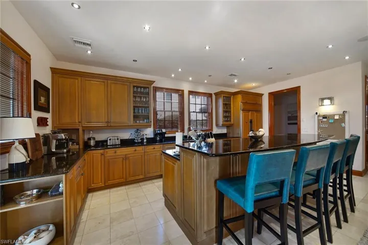 Kitchen sink & prep area at dbl windows, center island, dark stone counters, breakfast bar, and paneled Sub-Zero