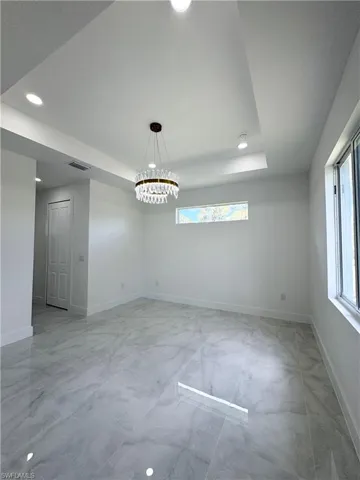 Empty room with a raised ceiling, recessed lighting, and a chandelier