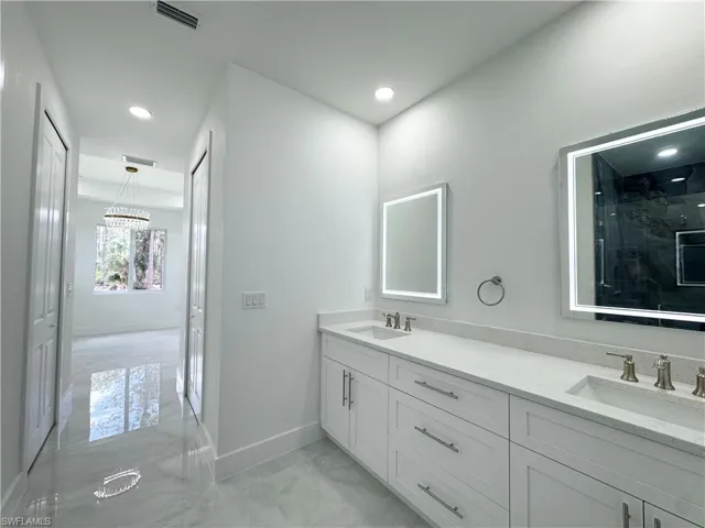 Full bathroom featuring a marble finish shower, double vanity, light marble finish floors, and recessed lighting