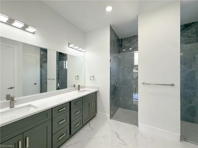 Full bath with a marble finish shower, double vanity, and light marble finish floors