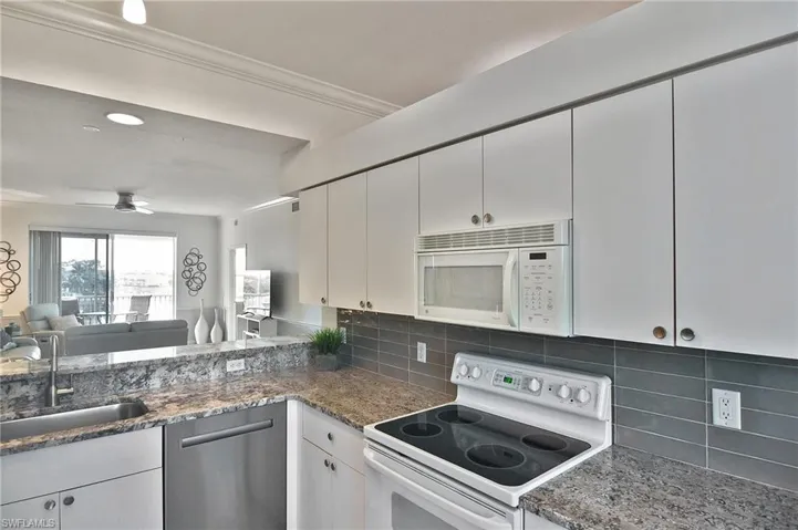Kitchen featuring white appliances, open floor plan, white cabinetry, dark stone counters, and ceiling fan