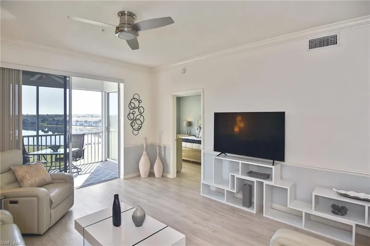 Living room featuring light wood finished floors, ceiling fan, crown molding, and a water view