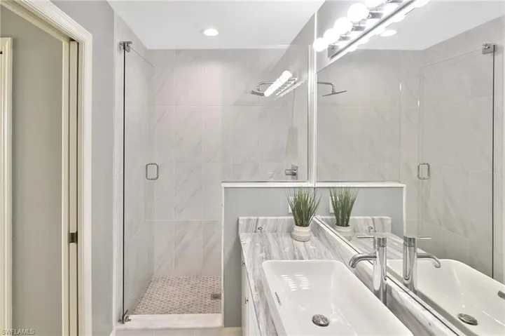 Bathroom featuring a stall shower, vanity, tile walls, and recessed lighting