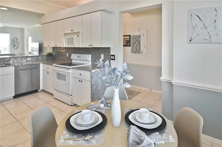 Kitchen with white appliances, tasteful backsplash, white cabinets, light tile patterned flooring, and crown molding