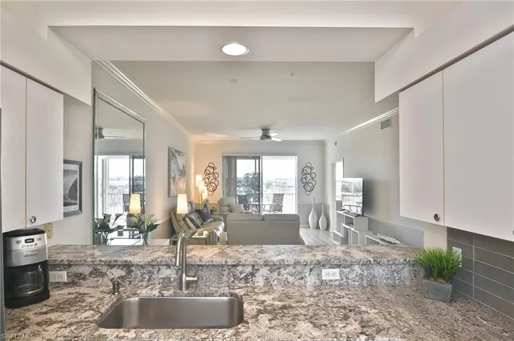 Kitchen featuring light stone counters, ornamental molding, white cabinetry, open floor plan, and ceiling fan