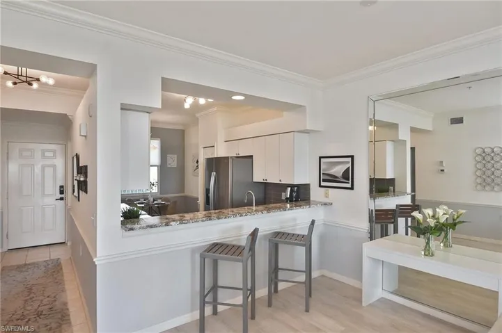 Kitchen featuring crown molding, a kitchen breakfast bar, stainless steel fridge, white cabinetry, and a peninsula