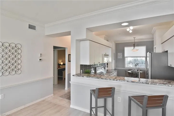 Kitchen with a breakfast bar, stainless steel appliances, white cabinets, crown molding, and decorative light fixtures