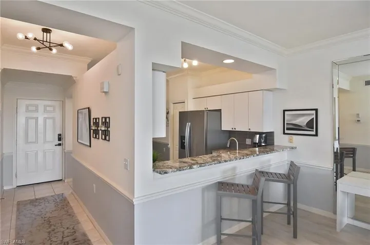 Kitchen featuring crown molding, a kitchen bar, white cabinetry, stainless steel fridge, and dark stone countertops
