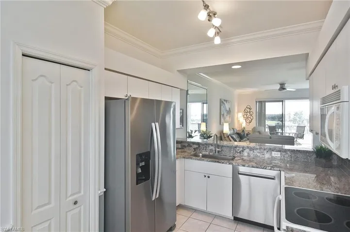 Kitchen featuring stainless steel appliances, open floor plan, crown molding, white cabinetry, and dark stone counters