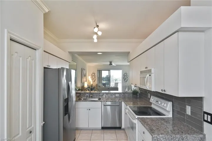 Kitchen with stainless steel appliances, ornamental molding, white cabinets, light tile patterned floors, and decorative backsplash