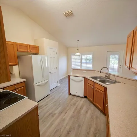 Kitchen featuring a peninsula, brown cabinetry, white appliances, light countertops, and pendant lighting
