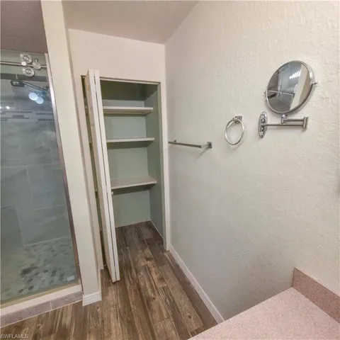 Full bath with a textured wall, a shower stall, dark wood-style floors, and a textured ceiling