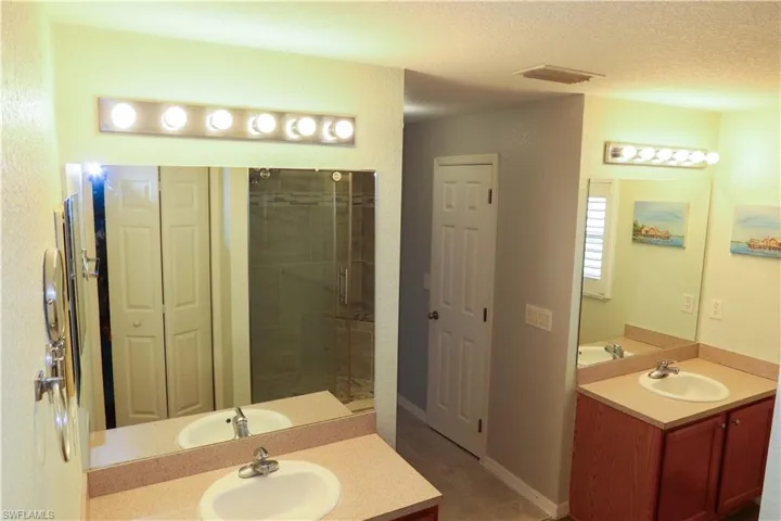 Full bath featuring a stall shower, two vanities, a textured ceiling, a textured wall, and light tile patterned floors