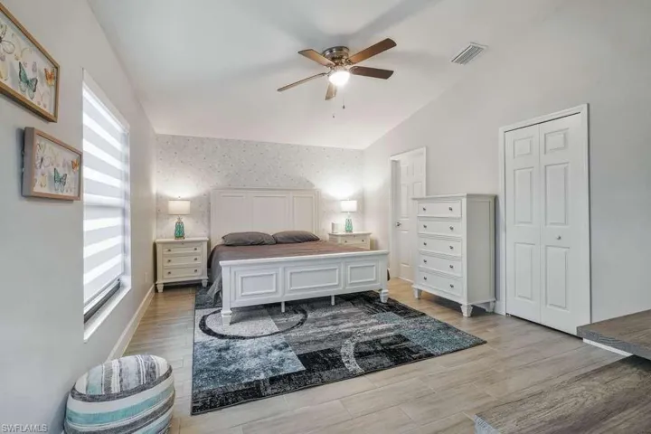 Bedroom with wallpapered walls, a ceiling fan, light wood-type flooring, and lofted ceiling