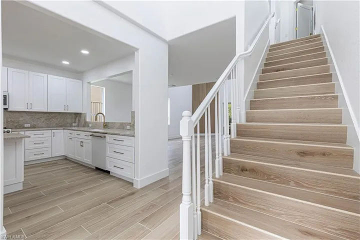 Kitchen featuring white appliances, light wood-style flooring, white cabinets, tasteful backsplash, and light stone counters