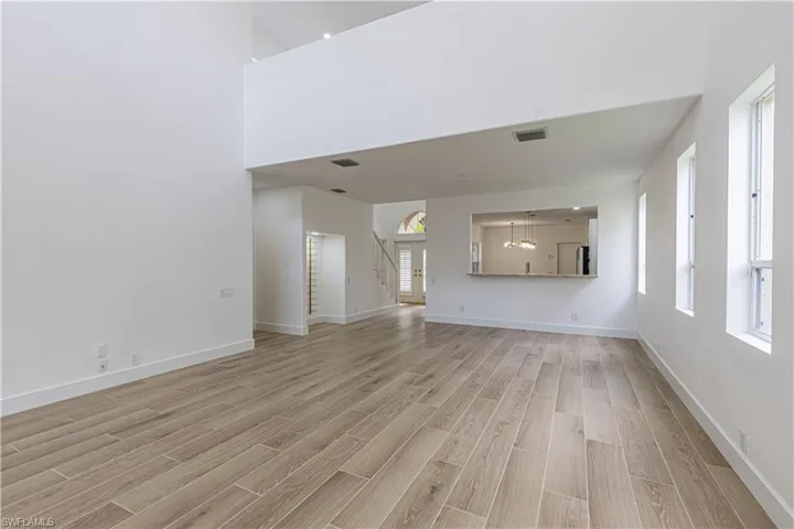Unfurnished living room featuring light wood-type flooring, stairs, healthy amount of natural light, and a high ceiling