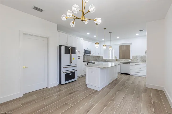Kitchen & appliances with gold and white finishes, white cabinets, a chandelier, light wood-type flooring, and recessed lighting