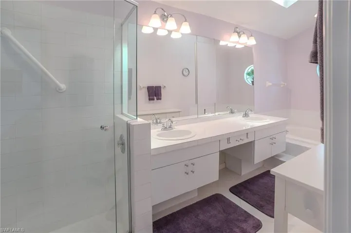 Full bathroom featuring double vanity, a stall shower, light tile patterned floors, a skylight, and a bath