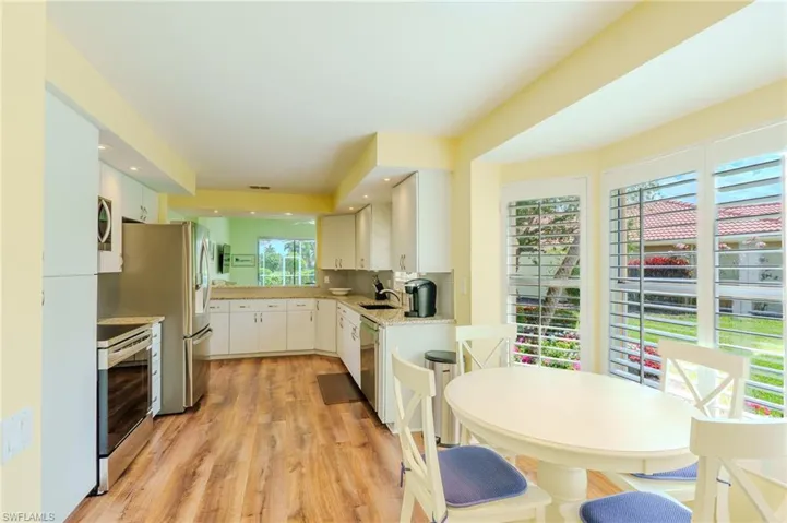Kitchen with stainless steel appliances, light wood-type flooring, light stone countertops, white cabinets, and decorative backsplash