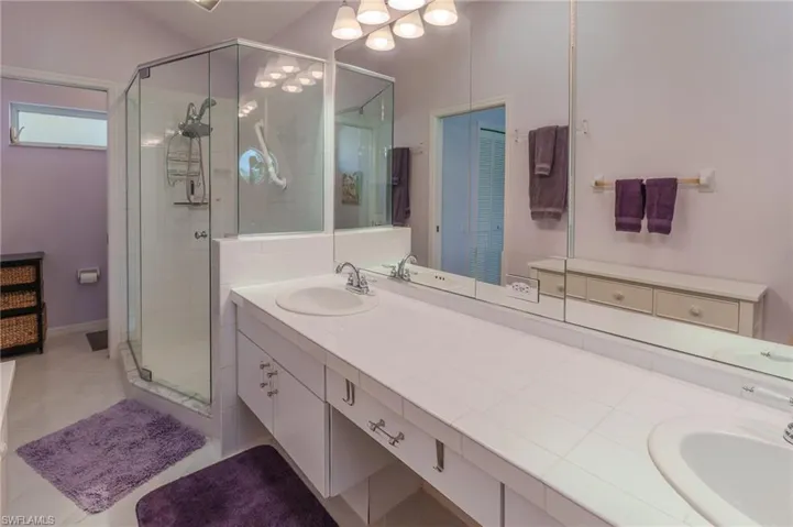 Full bath with a shower stall, double vanity, and light tile patterned flooring