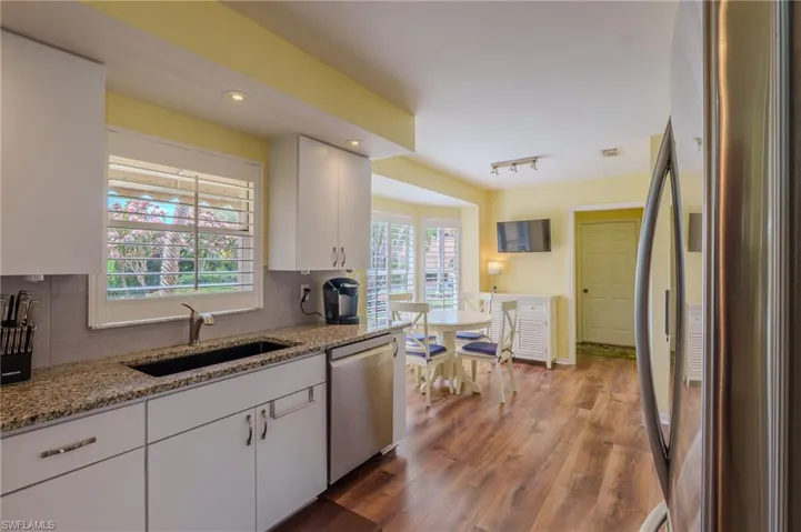 Kitchen with stainless steel appliances, white cabinets, decorative backsplash, light stone countertops, and dark wood finished floors