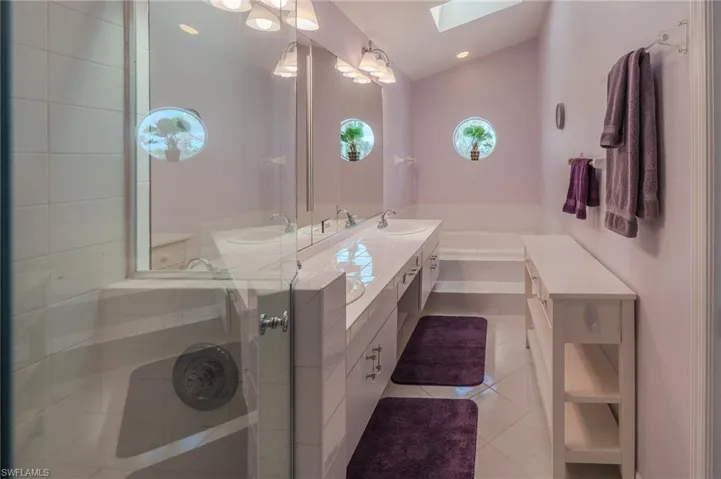 Bathroom featuring a skylight, a garden tub, vaulted ceiling, light tile patterned floors, and double vanity