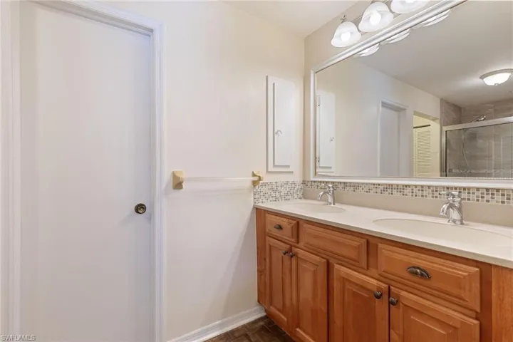 Bathroom featuring walk in shower, parquet flooring, vanity, and decorative backsplash