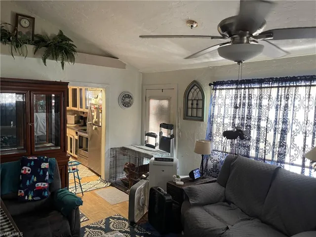 Living room with light wood-type flooring, ceiling fan, lofted ceiling, and a healthy amount of sunlight