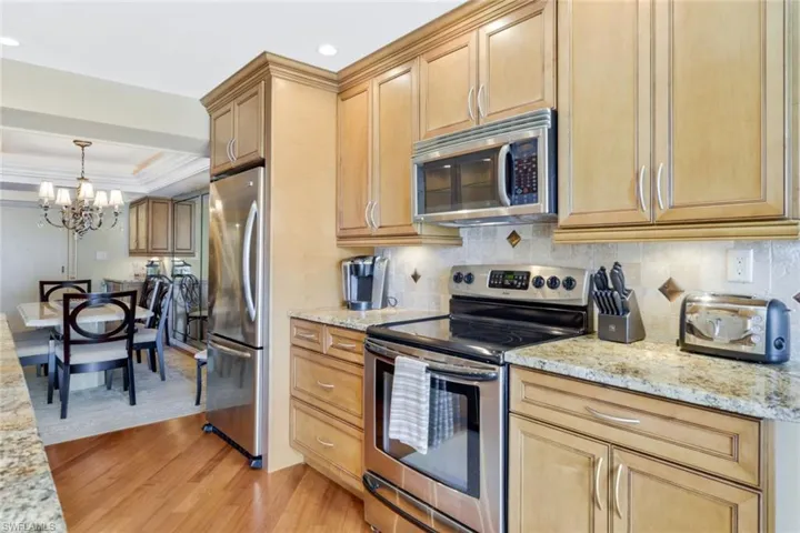 Kitchen featuring stainless steel appliances, an inviting chandelier, light stone countertops, and light wood-type flooring
