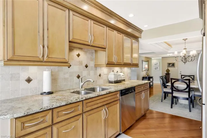 Kitchen featuring an inviting chandelier, light wood-type flooring, sink, tasteful backsplash, and stainless steel dishwasher