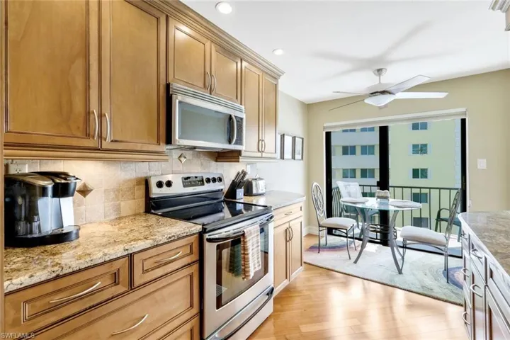 Kitchen with backsplash, light hardwood / wood-style flooring, light stone counters, stainless steel appliances, and ceiling fan